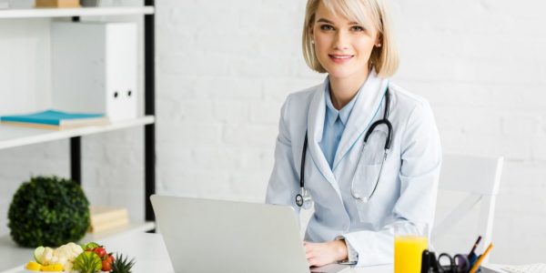cheerful-blonde-nutritionist-sitting-near-laptop-and-glass-of-fresh-orange-juice.jpg